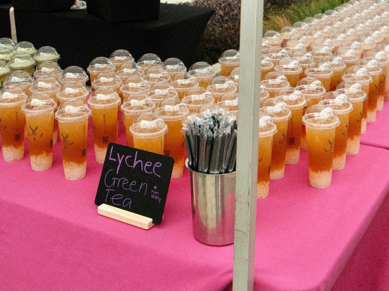 Rows of Lychee Green Tea cups on a pink table with a chalkboard sign