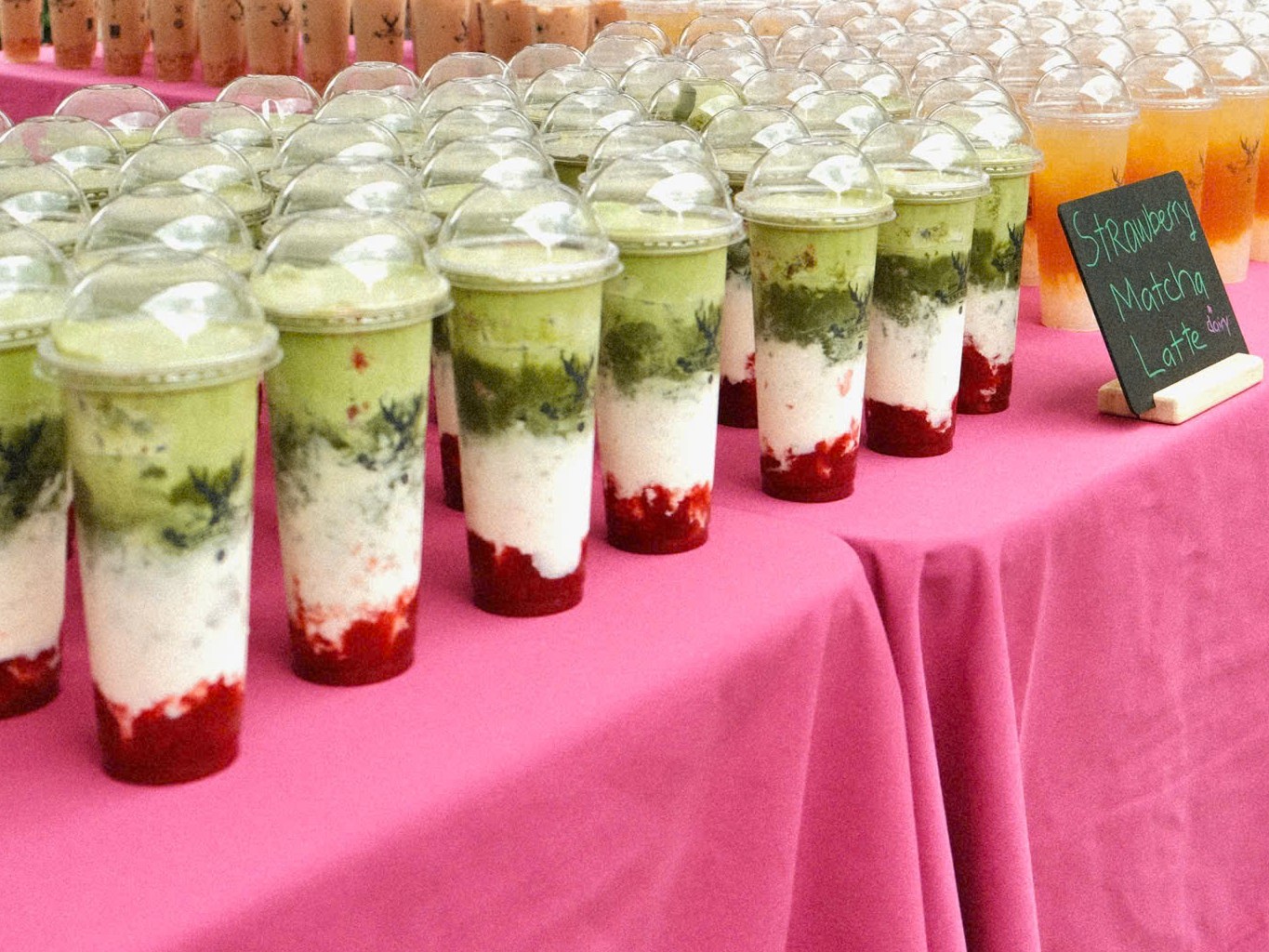 Layered Strawberry Matcha Latte cups lined up on a pink table
