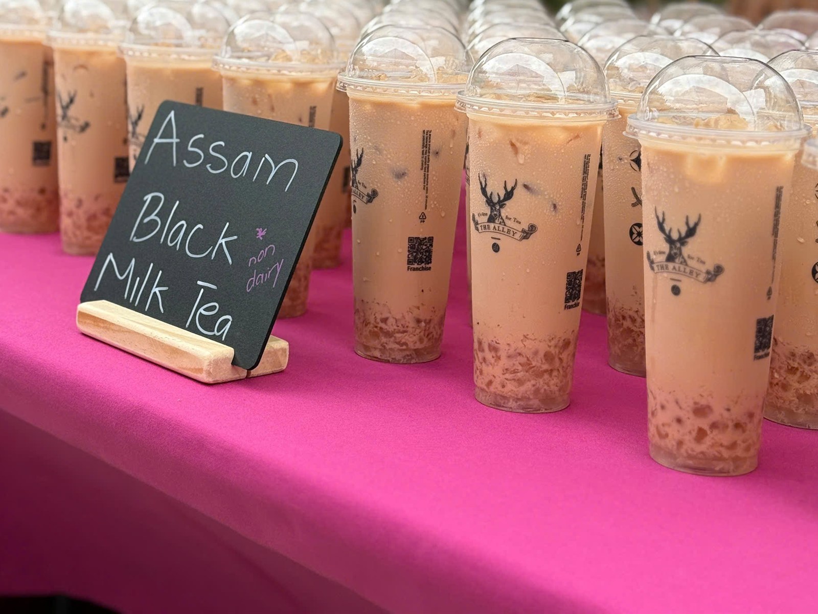 Cups of Assam Black Milk Tea with boba beside a chalkboard sign
