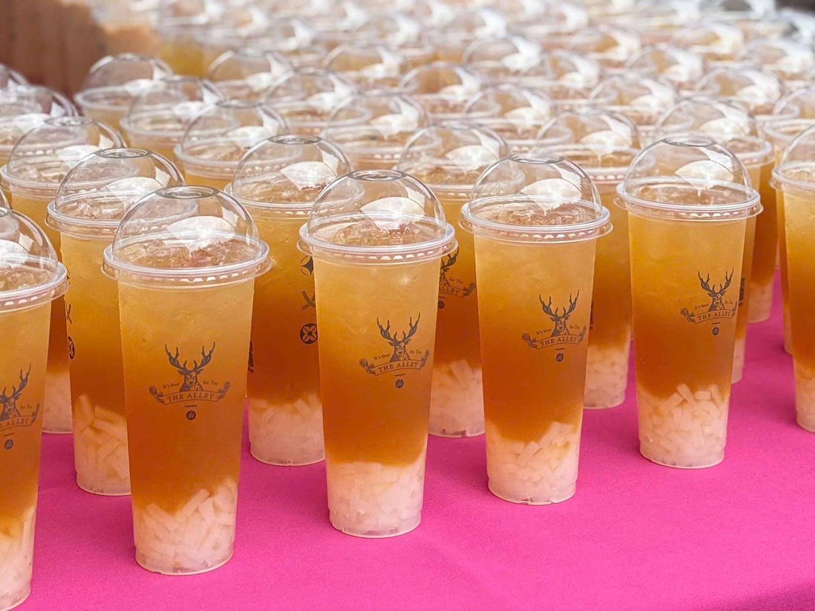 Fruit tea cups filled with boba, lined up in rows on a pink table
